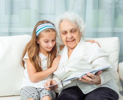 elderly woman with granddaughter with book on sofa