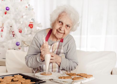 Elder woman soaking cream on Christmas baked cookies