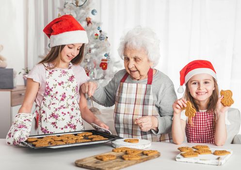 Grandmother with granddaughters in santa hats baking cookies