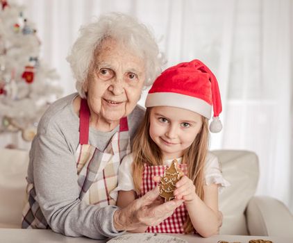 Grandmother with granddaughter in santa hat holding baked cookie