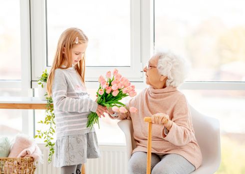 Nice little girl presenting bouquet to her grandmother in light room