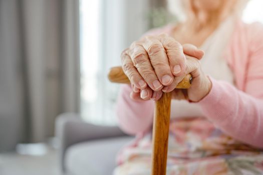 Senior woman hands holding wooden walking stick closeup. Pensioner elderly person portrait at home