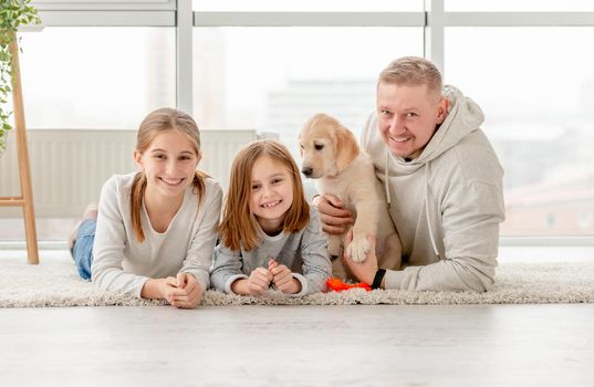 Smiling father with cute daughters and lovely puppy lying indoors