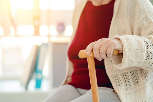 Wooden cane in hand of old woman sitting in light room