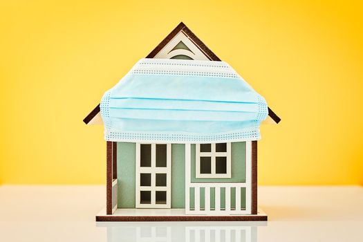 Model house wearing protective medical mask in yellow background