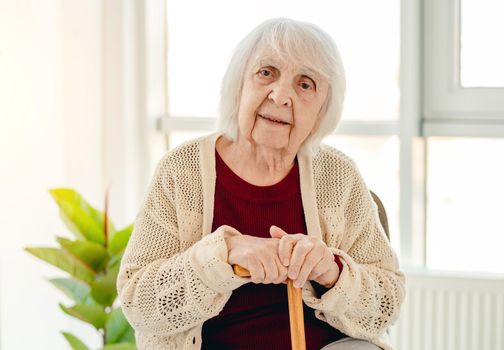 Portrait of elderly woman with wooden cane sitting in light room