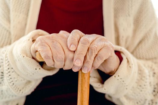 Wooden cane in hand of old woman sitting in light room