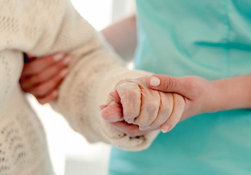 Close up view of old woman leaning on nurse while walking