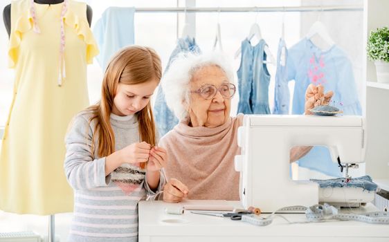 Elderly woman teaching little girl to sew in atelier