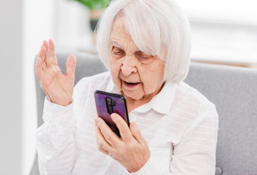 Elderly woman holding smartphone at her hand and looking at screen. Old generation and new technologies