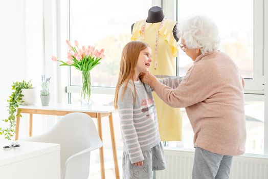Elderly woman taking measures of granddaughter indoors