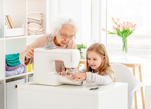 Lovely girl with granny sewing on machine in light room