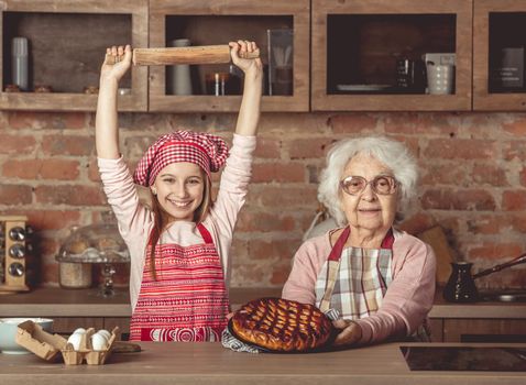 Cheerful grandaughter in chef uniform enjoyed the finished fruit pie with her granny