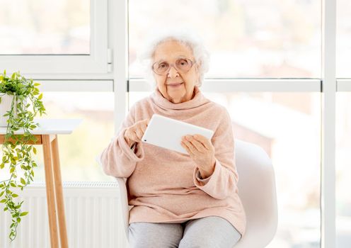 Aged woman in glasses with tablet at home