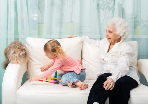 grandmother and granddaugter with cat on white sofa