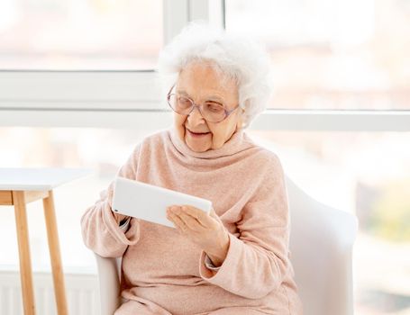 Aged woman in glasses with tablet at home