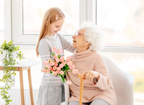 Nice little girl presenting bouquet to her grandmother in light room