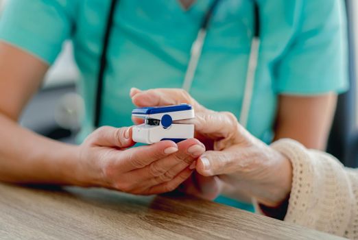 Doctor using pulse oximeter on old woman hand during appointment in clinic