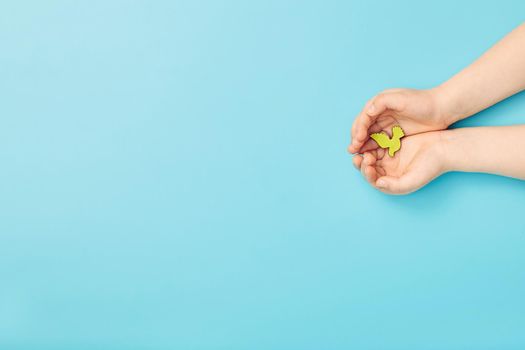 Сhild hands holding green dove bird on blue background, international day of peace or world peace day concept.