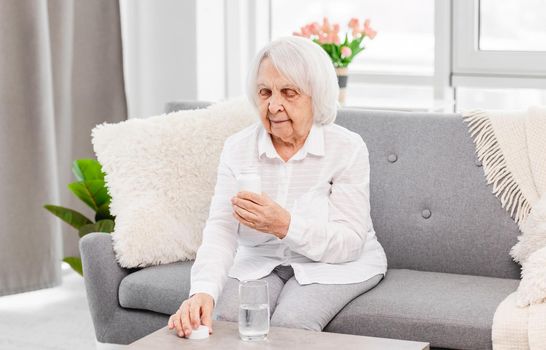 Eldery woman sitting on the sofa and looking at packaging of pills at home