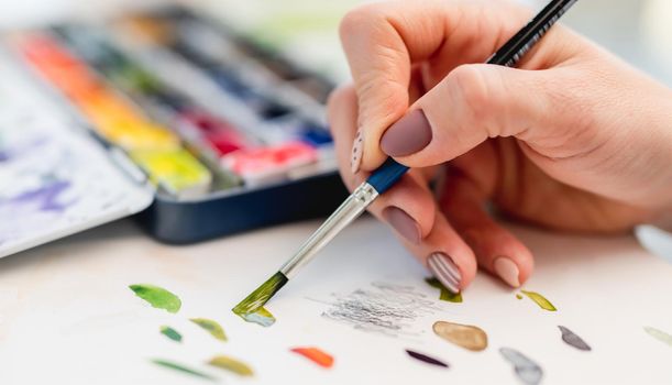 Hand of artist holding paintbrush and trying on white paper color of oaint