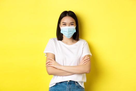 Covid, health care and pandemic concept. Asian woman in white t-shirt and medical mask cross arms on chest and looking at camera.