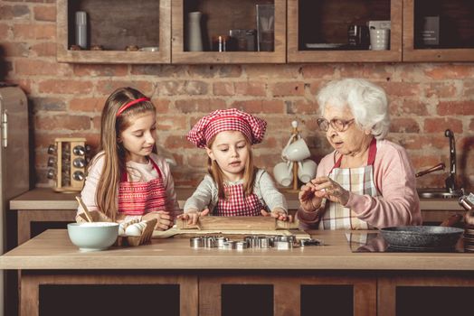 Grandma and granddaughters are spreading dough using a rolling pin