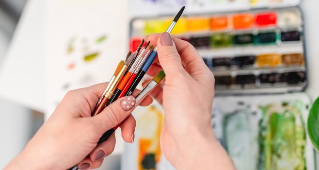 Woman artist hands holding paintbrushes and choosing one for drawing with watercolor