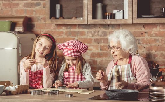 Two little granddaughters help granny to bake cookies at the rustic kitchen