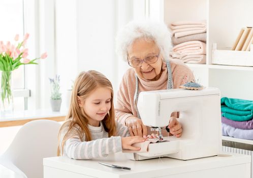 Grandmother teaching grandkid to sew on machine