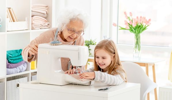 Lovely girl with granny sewing on machine in light room