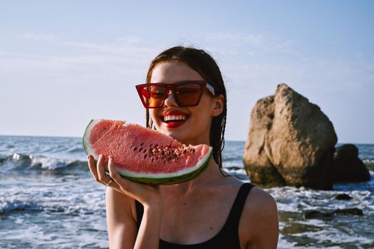 cheerful woman in black swimsuit eating watermelon on the beach. High quality photo