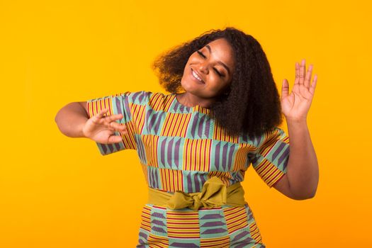 Young beautiful african american girl with an afro hairstyle. Portrait on yellow background with copyspace.