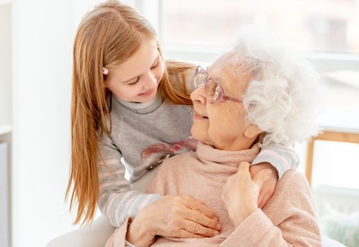 Lovely aged woman and little girl looking at each other at home