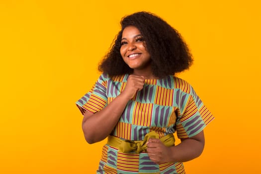 Young beautiful african american girl with an afro hairstyle. Portrait on yellow background with copyspace.