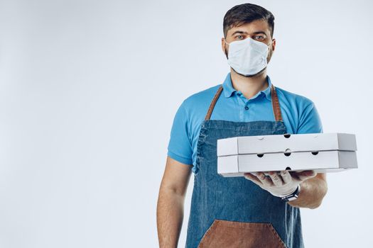 Pizza delivery man in medical gloves and mask against grey background. Safe service while coronavirus covid-19 outbreak