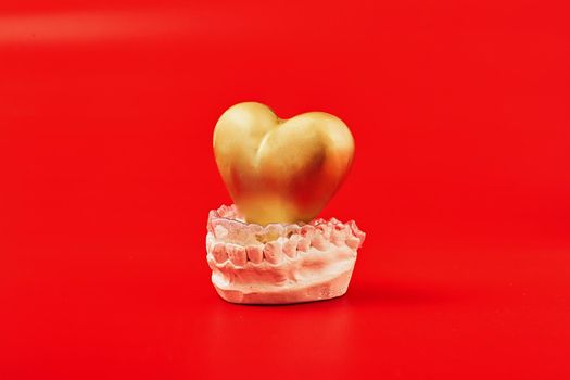 Heart of gold on a red background in invisible dental aligners or braces aplicable for an orthodontic dental treatment