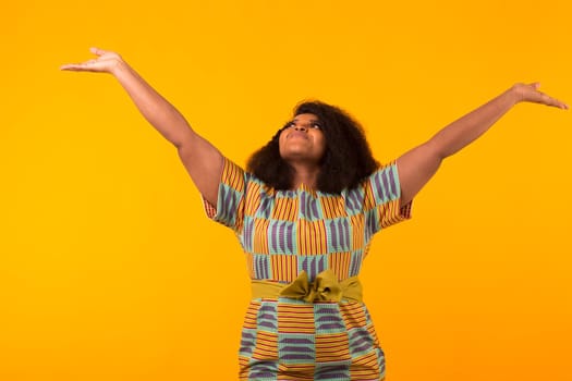 Happy beautiful african american girl with an afro hairstyle. Portrait on yellow background. Girl looking up.