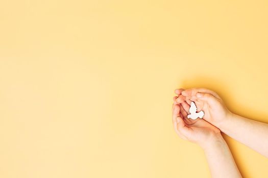 Сhild hands holding white dove bird on yellow background, international day of peace or world peace day concept.