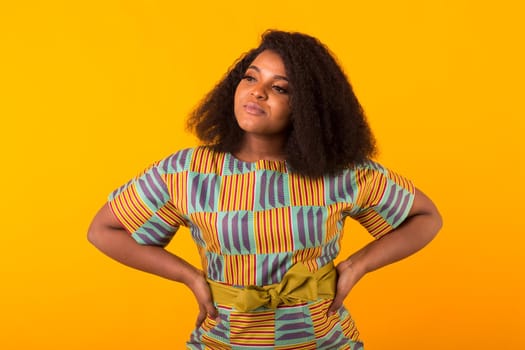 Young beautiful african american girl with an afro hairstyle. Portrait on yellow background with copyspace.