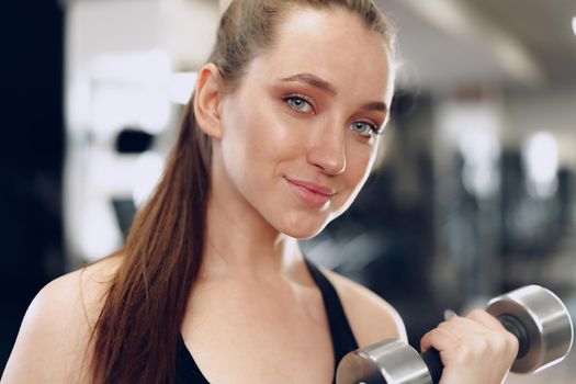 Young brunette sporty woman exercising with dumbbell in a gym close up
