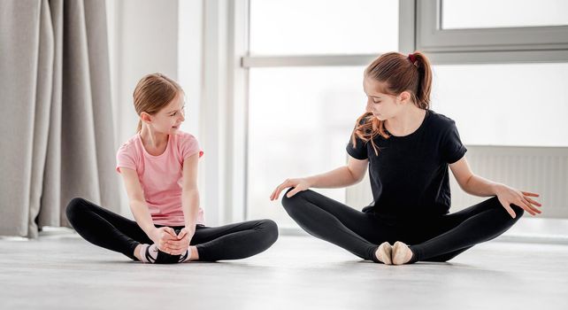 Two beautiful young girls making legs stretching sitting on the floor in butterfly position during ballet dance choreography class