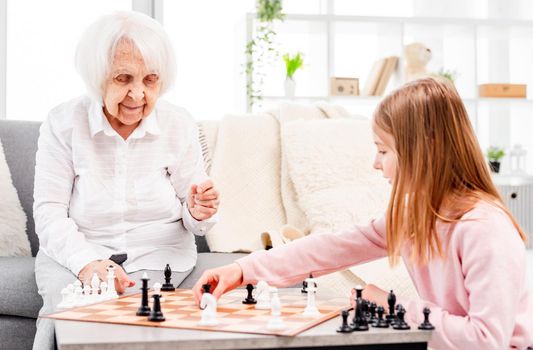Little beautiful girl playing chess with grandmother. Closeup family portrait
