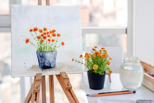 Wooden easel with drawing in artistic workspace in sunny day. White canvas with flowers painted from nature