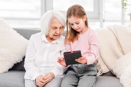 Grandaughter shows to her grandmother something on tablet. Concept of generations and technologies