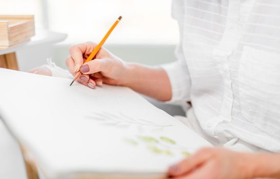 Woman drawing sketch on white paper canvas holding yellow pencil in her hand