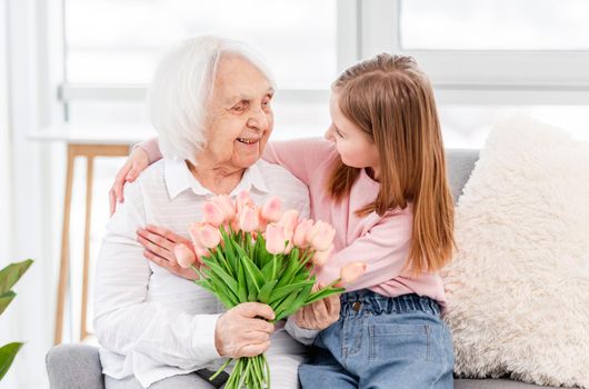 Grandmother with tulips flowers in her hands with preschool grandaughter hugging and lookint at each other