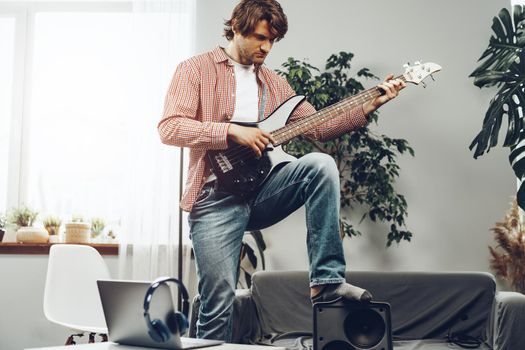 Man playing electric guitar and recording music into laptop at home