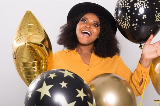 Portrait of smiling young African-American adult woman looking sweet on yellow background holding balloons.