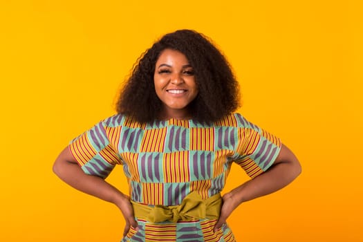 Young beautiful african american girl with an afro hairstyle. Portrait on yellow background with copyspace.